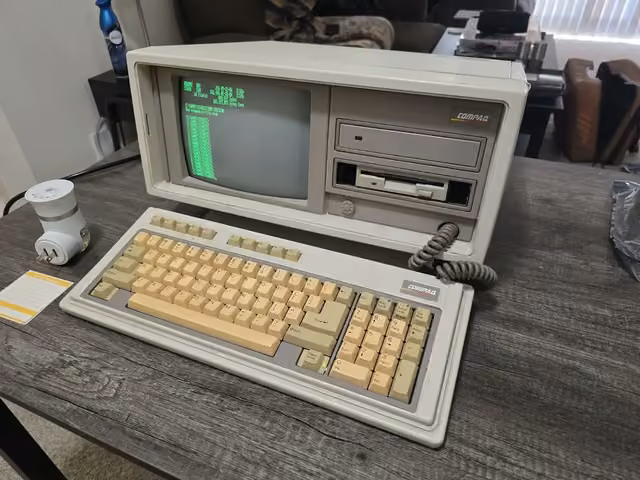 Compaq Portable vintage computer with keyboard attached, showing a DOS directory listing on its built-in CRT screen